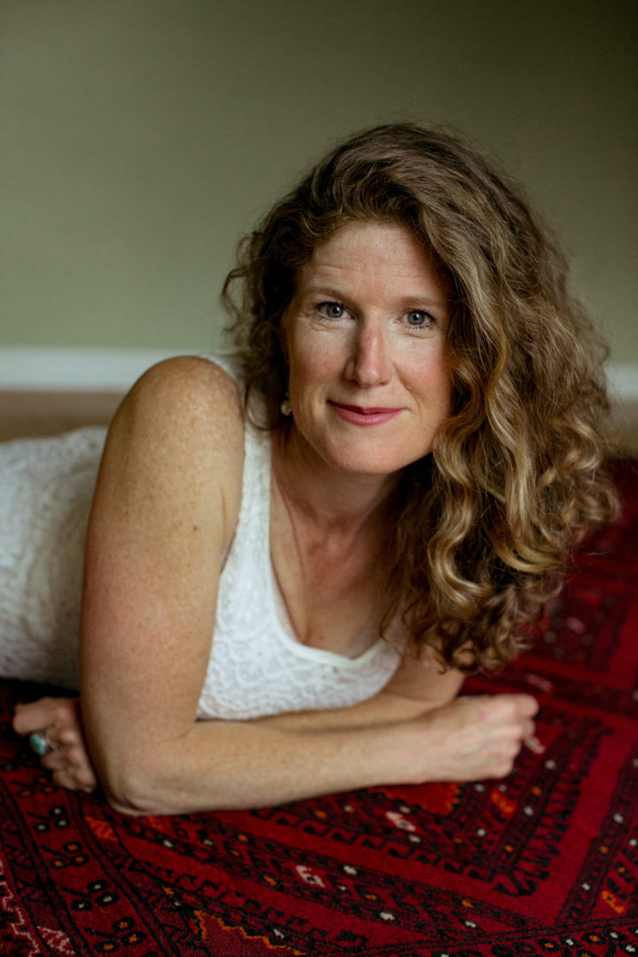 sarah belzile lounging on furniture covered in red silk. she smiles and looks at the camera softly.